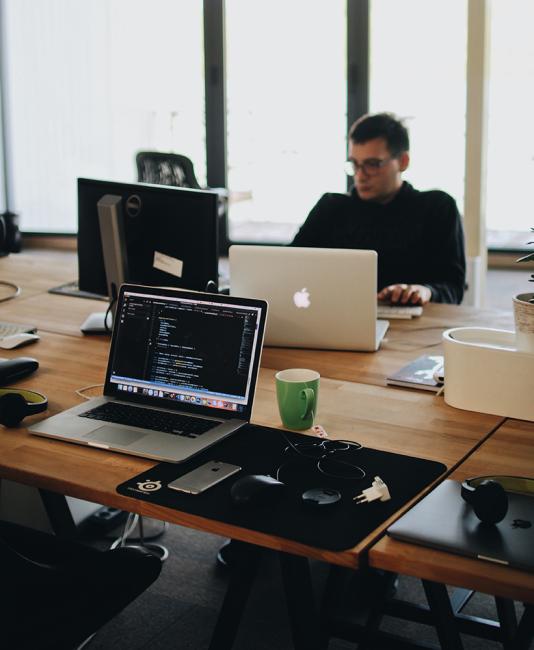 Man in Black Shirt Sits Behind Desk With Computers